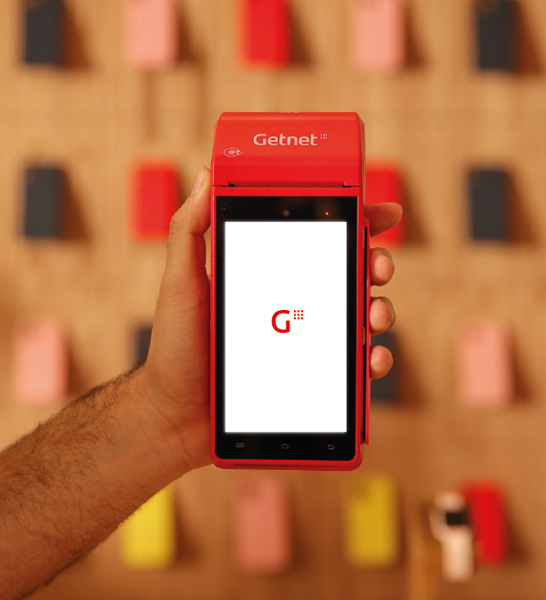 Mano sosteniendo una terminal roja de Getnet con pantalla encendida mostrando el logo de Getnet