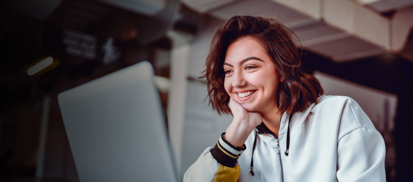 Persona con campera clara y detalles oscuros sentada frente a una computadora portátil.