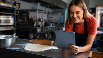 Persona en una cocina profesional usando una tablet junto a una masa estirada y un palo de amasar.