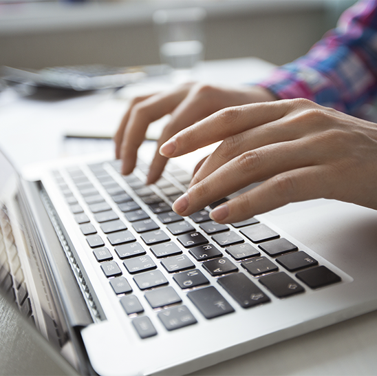 Manos escribiendo en el teclado de una computadora portátil sobre un escritorio.
