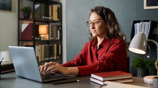 Persona trabajando en una notebook, frente a un escritorio con libros y elementos de trabajo.