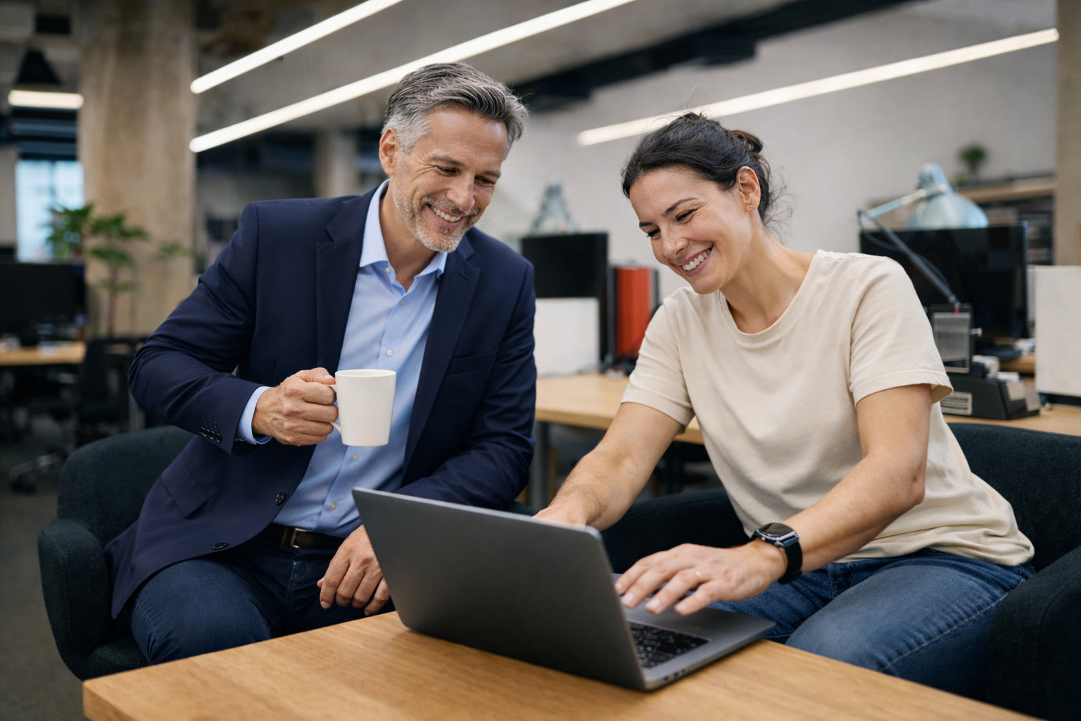 Dos personas en una oficina revisan información en una computadora portátil sobre un escritorio.