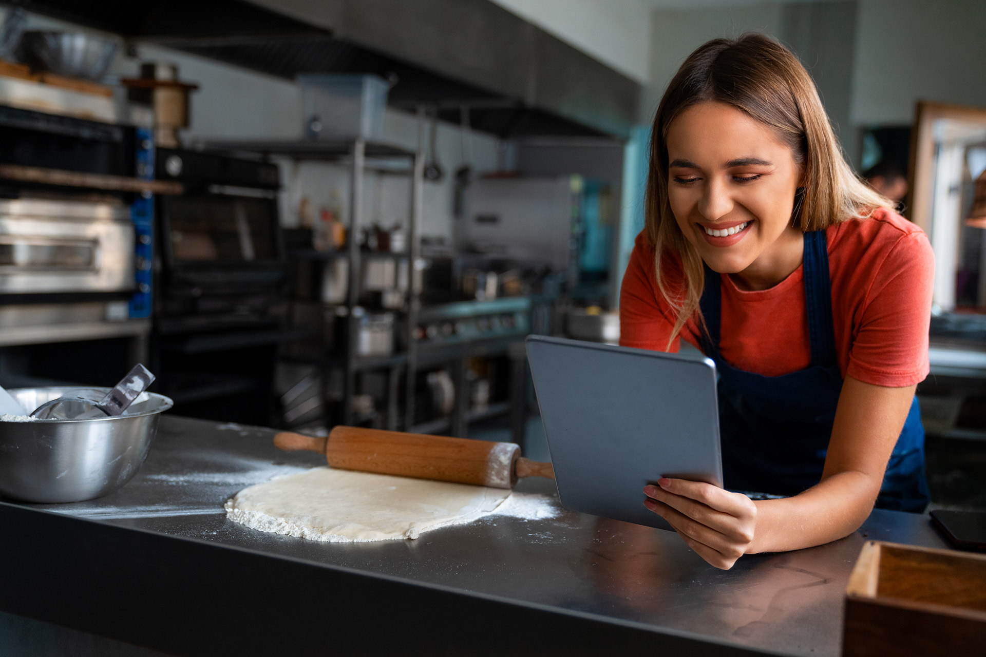 Persona en una cocina profesional usando una tablet junto a una masa estirada y un palo de amasar.